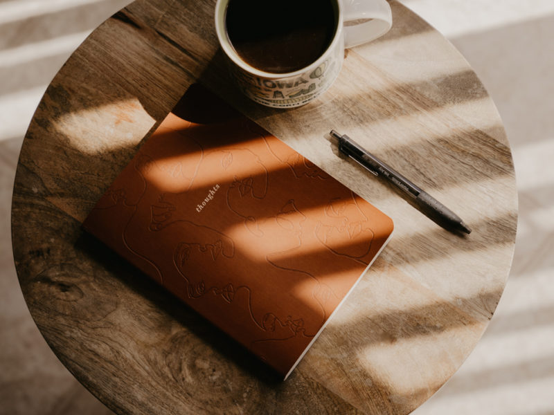 Journal next to a pen and cup of coffee